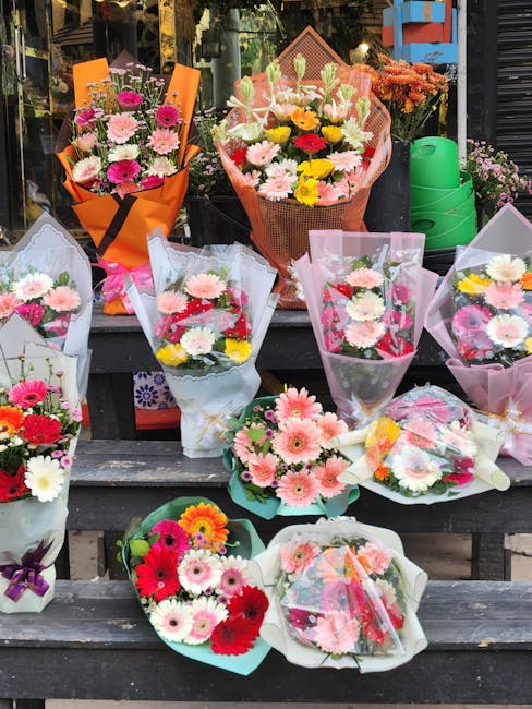 A display of various fresh flower bouquets arranged on outdoor wooden steps outside a florist shop. The bouquets feature vibrant pink, white, yellow, and red gerbera daisies, roses, and chrysanthemums